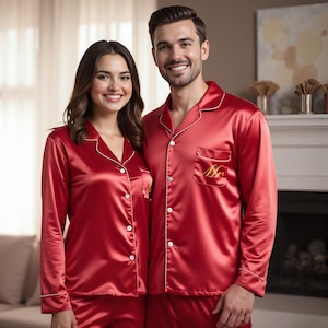 May include: A couple wearing matching red satin pyjamas with white piping. The man's pyjamas have "Mr." embroidered on the pocket.