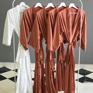 a collection of four robes hanging on a rack, with three of them being brown and one being white.