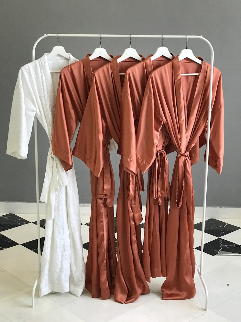 a collection of four robes hanging on a rack, with three of them being brown and one being white.