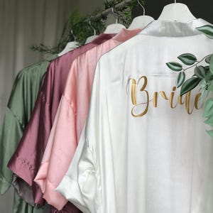 A row of colorful robes or bathrobes hanging on a clothing rack, with the word "Bride" printed on the back of one of the robes.
