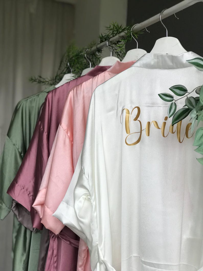 A row of colorful robes or bathrobes hanging on a clothing rack, with the word "Bride" printed on the back of one of the robes.