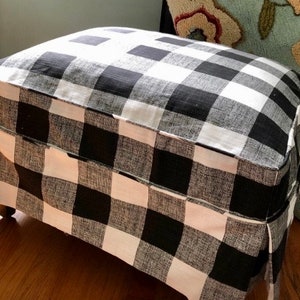 May include: Black and white checked fabric ottoman with a pleated skirt. The ottoman is made of a soft, textured fabric.