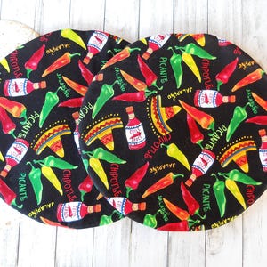 May include: Three black round fabric pot holders with a repeating pattern of red and green chili peppers, yellow and green jalapenos, and a sombrero with the words "Jalapeno", "Chipotle", and "Picante" on each.