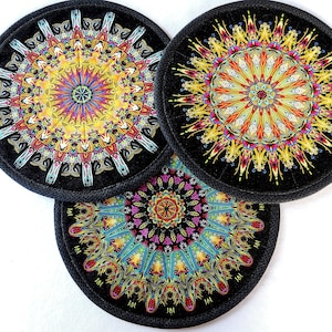 May include: Three round black coasters with colorful mandala designs. Each coaster features a different pattern with intricate details in shades of yellow, red, blue, and green.