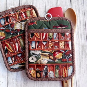 May include: Two brown and green pot holders with a fishing lure pattern. The pot holders have a loop for hanging.