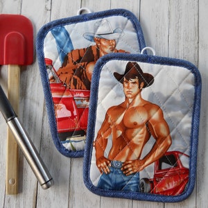 May include: Two denim-trimmed pot holders with a quilted white background. Each pot holder features a different image of a man wearing a cowboy hat and jeans. One man is leaning against a red truck, while the other man is standing with his hands on his hips.