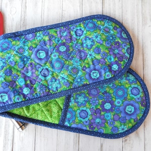 May include: A pair of blue and green floral oven mitts with a navy blue trim. The mitts are quilted and have a green lining.