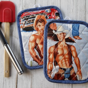 May include: Two blue denim pot holders with a quilted design. Each pot holder features a different image of a shirtless cowboy wearing a cowboy hat. The cowboys are standing in front of a red pickup truck and a desert landscape.