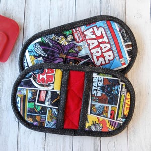 May include: Two Star Wars-themed oven mitts with a comic book design. The mitts feature images of Darth Vader and other characters, with the words "Star Wars" prominently displayed. They have a red center panel and a black dotted border.