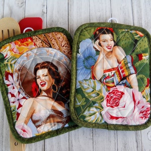 May include: Two green quilted pot holders with a floral design featuring women in vintage clothing. One pot holder has a woman wearing a large hat and the other has a woman wearing a colorful shawl.