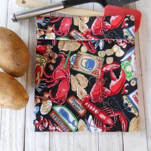 May include: A black reusable grocery bag with a colorful print of lobsters, crabs, and other seafood. The bag has the words "Lobster Bisque" and "Steamers Fight" printed on it.