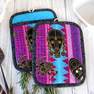 May include: Two purple, blue, and pink quilted pot holders with black trim and gold African-inspired designs.