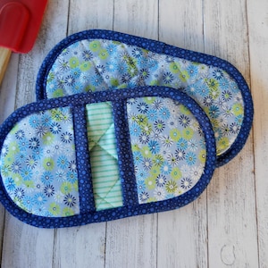May include: Two blue and white floral oven mitts with a green and white striped center panel. The mitts are quilted and have a blue trim.