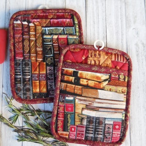 May include: Two red quilted pot holders with a book print design. The pot holders have a loop for hanging.