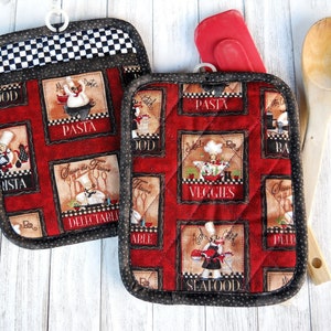 May include: Two red quilted pot holders with black trim and a checkered black and white lining. The pot holders feature a repeating pattern of chefs and food-related words like "Pasta", "Veggies", and "Seafood".