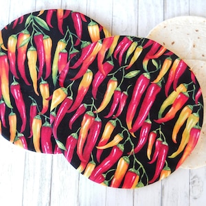 May include: Two round black fabric placemats with a red and yellow chili pepper pattern. The placemats are on a white wooden surface.