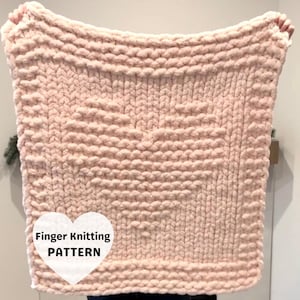 Peut inclure: Une couverture rose clair tricotée aux doigts avec un motif de cœur au centre. La couverture est faite de fil épais et a un aspect texturé. Les mots "Finger Knitting PATTERN" sont dans un cœur blanc.