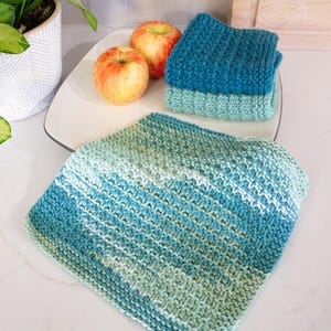 May include: Three square crocheted washcloths featuring a textured stitch pattern. One cloth displays a variegated gradient of teal, blue, and light green, while the other two are solid colors in dark teal and light seafoam green respectively.