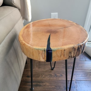 May include: A wooden end table with a natural wood finish and a dark blue resin inlay. The table has three black hairpin legs.