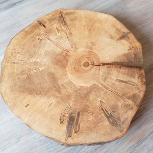May include: A round wooden slice with a natural wood grain pattern and a dark brown center. The wood has a light brown color and a smooth surface.