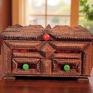 May include: A handcrafted wooden box with a textured, layered design. The box features a red and green knob, and a red interior. The box is brown with a decorative, geometric pattern.