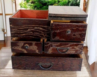 May include: A dark brown wooden chest with five drawers. The top drawer is open and the chest has a lid that is also open. The chest has a rustic look and is made of wood with a natural grain.