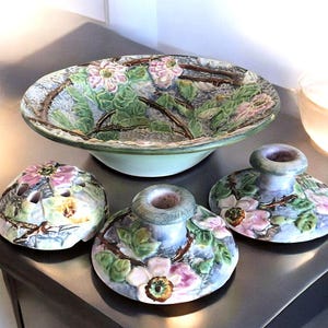 May include: A set of three vintage ceramic candle holders and a bowl, all featuring a floral design with pink flowers and green leaves.