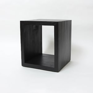 May include: A black wooden cube shelf with an open front. The shelf is made of thick planks of wood and has a rustic look.