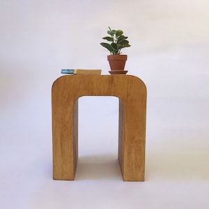May include: A wooden side table with a unique arch shape. The table has a natural wood finish and is topped with a small potted plant.