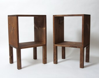 May include: Two wooden end tables with a square top and four legs. The tables are made of dark brown wood and have a simple, rustic design.