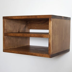 May include: A rectangular wall-mounted wooden shelf unit featuring a dark brown stained finish with visible wood grain. The structure consists of a top panel, a bottom panel, two side panels, and a single horizontal middle shelf, creating two open storage compartments.