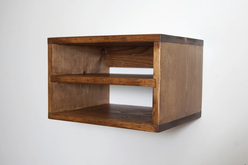 May include: A rectangular wall-mounted wooden shelf unit featuring a dark brown stained finish with visible wood grain. The structure consists of a top panel, a bottom panel, two side panels, and a single horizontal middle shelf, creating two open storage compartments.