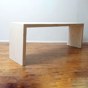 May include: A simple, white wooden bench with a rectangular top and a minimalist design. The bench is made of unfinished wood and has a natural, rustic look.