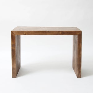 May include: A rectangular wooden table with a dark brown stained finish and a visible wood grain pattern. The table features a simple waterfall design with two vertical side panels supporting a flat horizontal top surface, creating a clean structure.