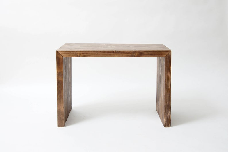 May include: A rectangular wooden table with a dark brown stained finish and a visible wood grain pattern. The table features a simple waterfall design with two vertical side panels supporting a flat horizontal top surface, creating a clean structure.