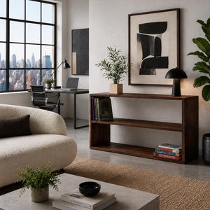 May include: A rectangular dark wood console table featuring two open shelves. The top shelf holds a small potted plant and a black mushroom-shaped lamp, while the bottom shelf contains a stack of books. The table has a smooth, flat surface.