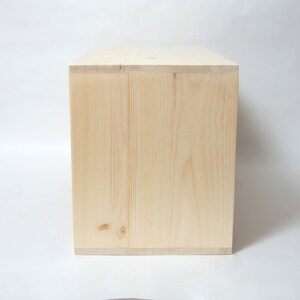 May include: A rectangular wooden box made of light-colored, unfinished pine wood. The box features visible wood grain patterns, natural knots, and clean, straight edges. The construction shows clear joinery where the side panels meet the top.