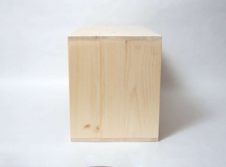May include: A rectangular wooden box made of light-colored, unfinished pine wood. The box features visible wood grain patterns, natural knots, and clean, straight edges. The construction shows clear joinery where the side panels meet the top.