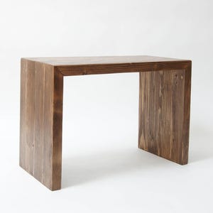 May include: A dark brown wooden table with a simple, rectangular design. The table has a square top and four legs, each made of a single piece of wood. The table is made of reclaimed wood and has a rustic, industrial look.