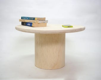 May include: A light wood oval table with a cylindrical base. The table has a stack of books and a green phone on top.