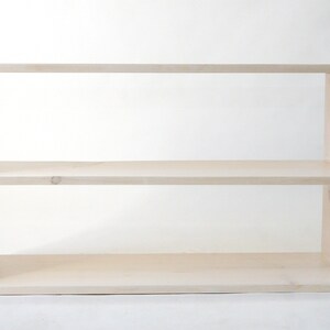 May include: A rectangular, light-colored wooden shelf unit featuring two horizontal tiers. The structure is composed of a top panel, a bottom panel, two side panels, and a single middle shelf, creating two open storage compartments with a smooth finish.
