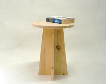May include: A light wood side table with a round top and a unique, angled, three-legged base. A book titled "Moore" is resting on the table.