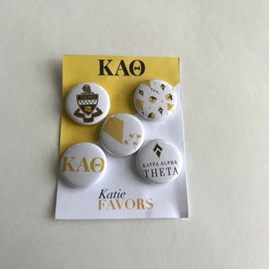 May include: Five white round buttons with gold lettering and designs. The buttons feature the Greek letters "KAO", a crest, a kite, a geometric pattern, and the words "Kappa Alpha Theta". The buttons are displayed on a white card with the words "KAO" and "Katie Favors" printed in black.