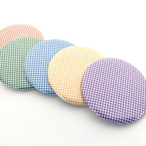 May include: Five round, fabric-covered objects in a row, each with a gingham pattern. The colors are red, green, blue, yellow, and purple. The objects are arranged diagonally against a white background.