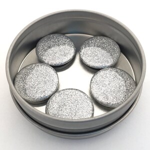 May include: Five silver glitter round magnets in a silver tin container.