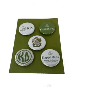 May include: Five round green and white buttons with different Kappa Delta sorority logos. The logos include the letters "KD", a crest, and the words "Kappa Delta" with the tagline "Building Confidence, Inspiring Action".