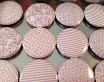 Può includere: Una collezione di 12 bottoni rotondi con motivi viola e bianchi. I bottoni presentano una varietà di disegni geometrici e floreali.
