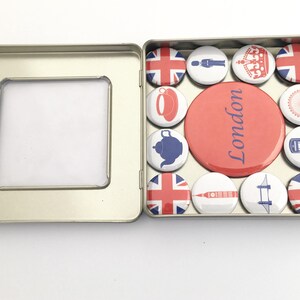 Puede incluir: Una caja de hojalata con una ventana transparente, que contiene un conjunto de 12 botones redondos con tem&aacute;tica londinense. Los botones presentan im&aacute;genes de la bandera de la Union Jack, una corona, una tetera, un autob&uacute;s de dos pisos rojo, el Big Ben, el London Eye y las palabras "Londres".
