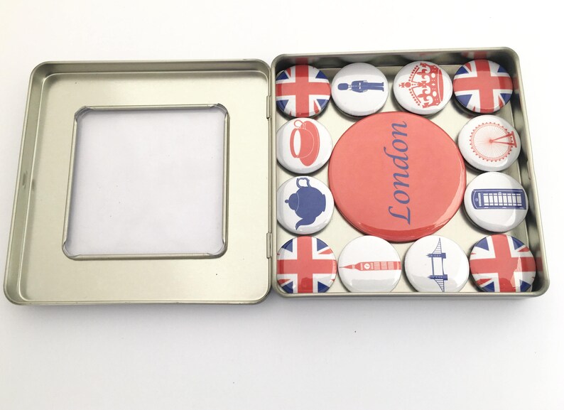 Puede incluir: Una caja de hojalata con una ventana transparente, que contiene un conjunto de 12 botones redondos con tem&aacute;tica londinense. Los botones presentan im&aacute;genes de la bandera de la Union Jack, una corona, una tetera, un autob&uacute;s de dos pisos rojo, el Big Ben, el London Eye y las palabras "Londres".