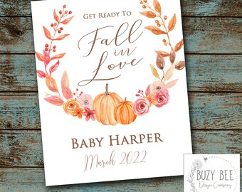 May include: A white print with the text "Get Ready to Fall in Love" and "Baby Harper March 2022". The design features a watercolour wreath with pumpkins and flowers in shades of orange, pink, and brown. A logo for "BUZY BEE Design Company" is in the corner.